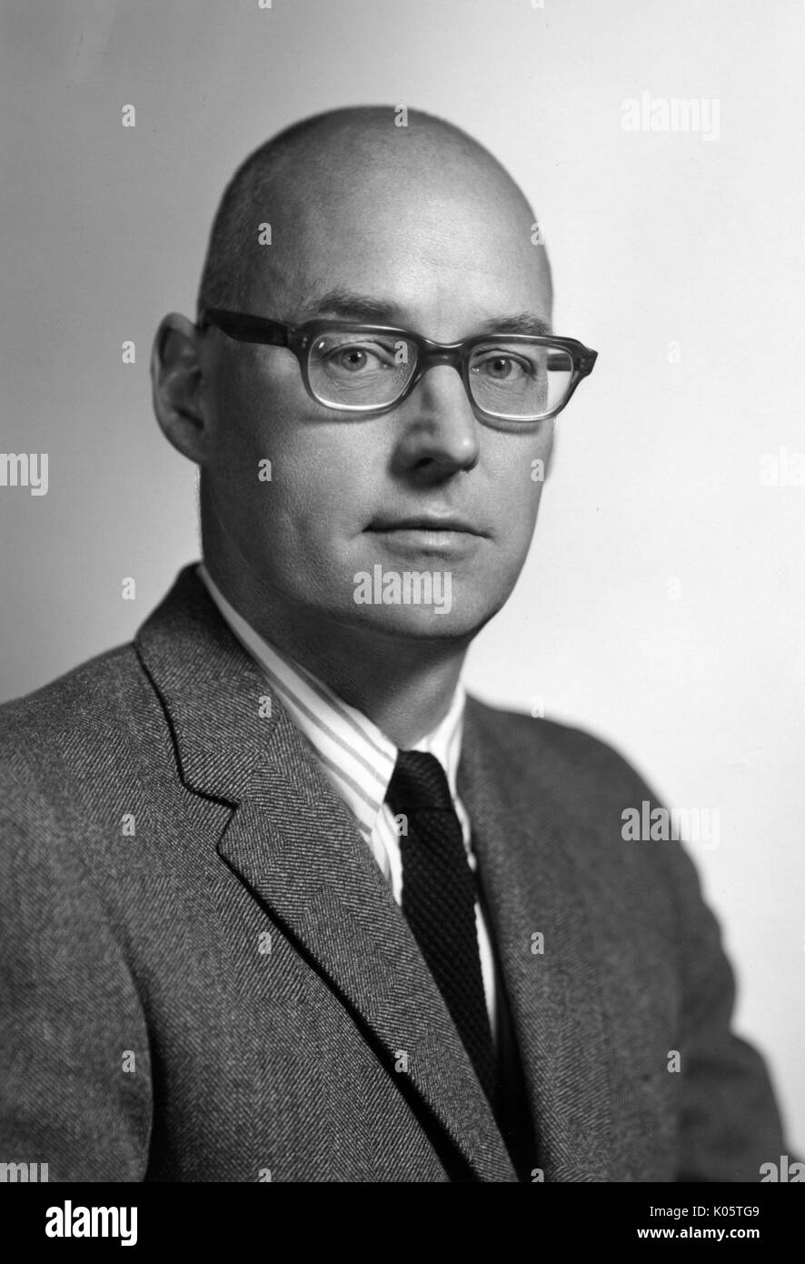 Half-length portrait of American historian of science Dr Charles C Gillispie, wearing a dark suit and a dark tie with a striped shirt, with a serious facial expression, wearing dark glasses, posed in front of a backdrop, 1965. Stock Photo