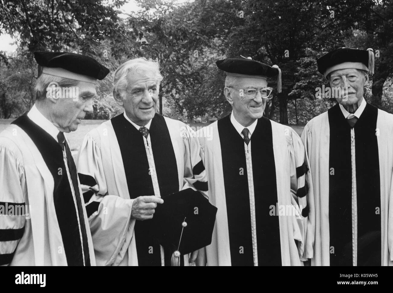 Half-length portrait of four men at Johns Hopkins commencement, all sporting cap and gown, standing outside, mostly smiling facial expressions, from left to right: Daniel K Ludwig, American composer and pianist Leonard Bernstein, Jules Stein, and Edward O Hulburt, 1980. Stock Photo