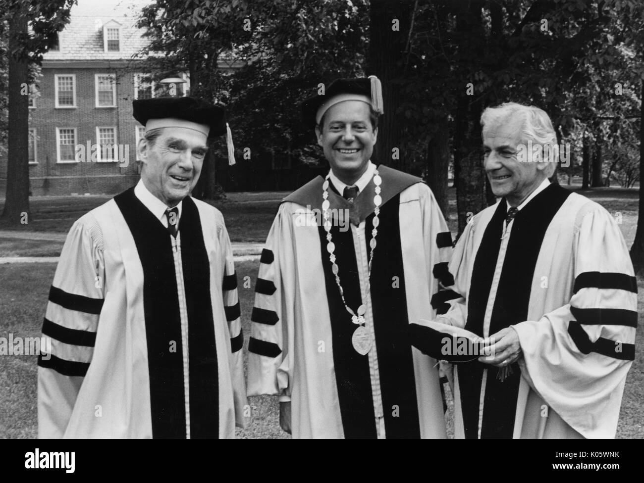 Half-body portrait of three men at 1980 Johns Hopkins commencement, all in cap and gown attire, from left to right: Professor Daniel K Ludwig, President Steven Muller, and musician Leonard Bernstein, who has removed his hat and drawn the other two's attention towards him, 1980. Stock Photo