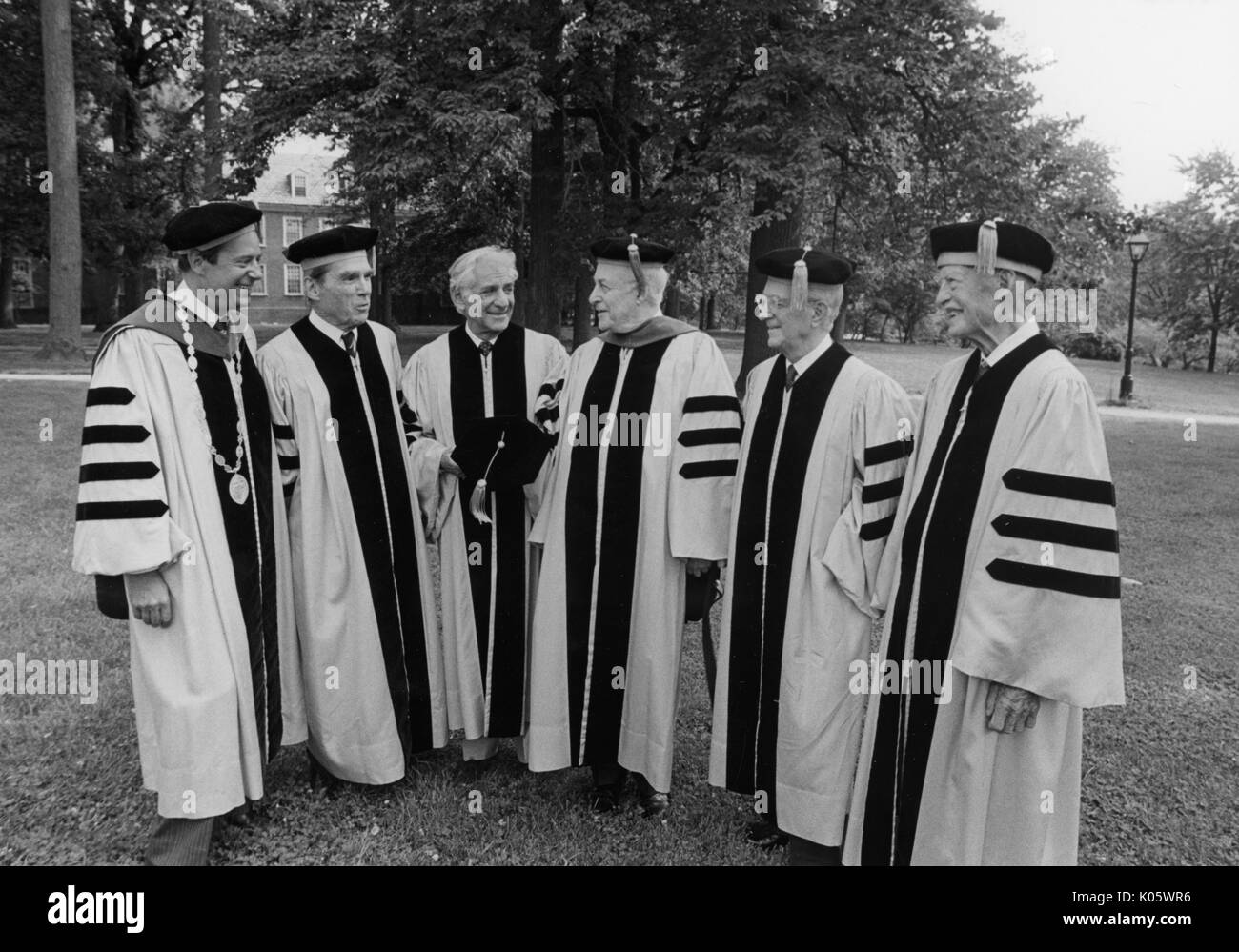 Full-body portrait of President Steven Muller, Professor Daniel K Ludwig, musician Leonard Bernstein, and Professor Milton Reder, and two others in cap and gown on a college quad for Johns Hopkins 1980 Commencement, 1980. Stock Photo