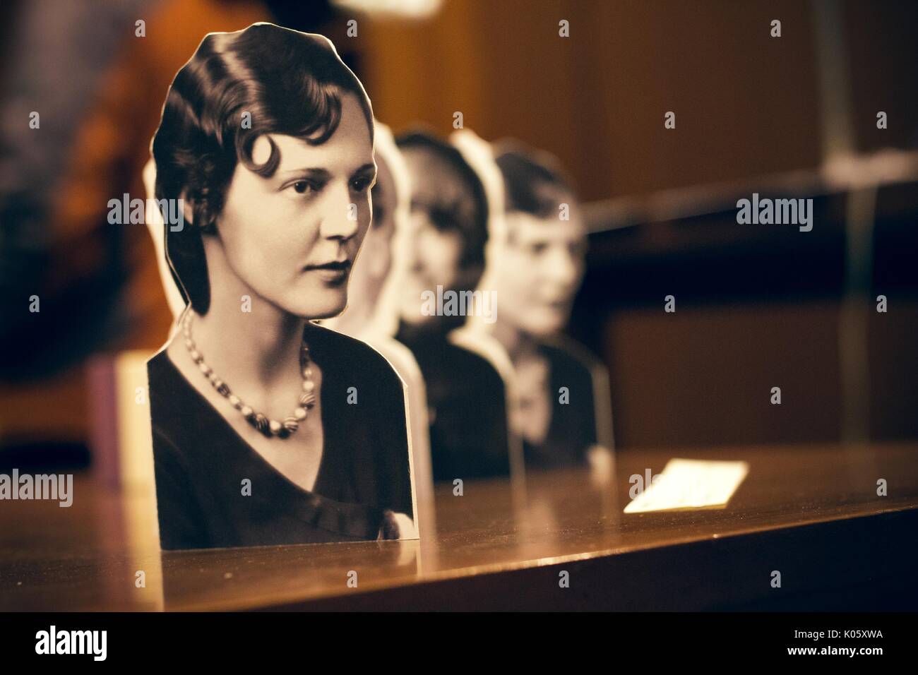 A black and white paper cut-out of a portrait of a dark-haired woman wearing a necklace, with several similar cut-outs in a diagonal row behind this one, propped on a wooden table, 2016. Stock Photo