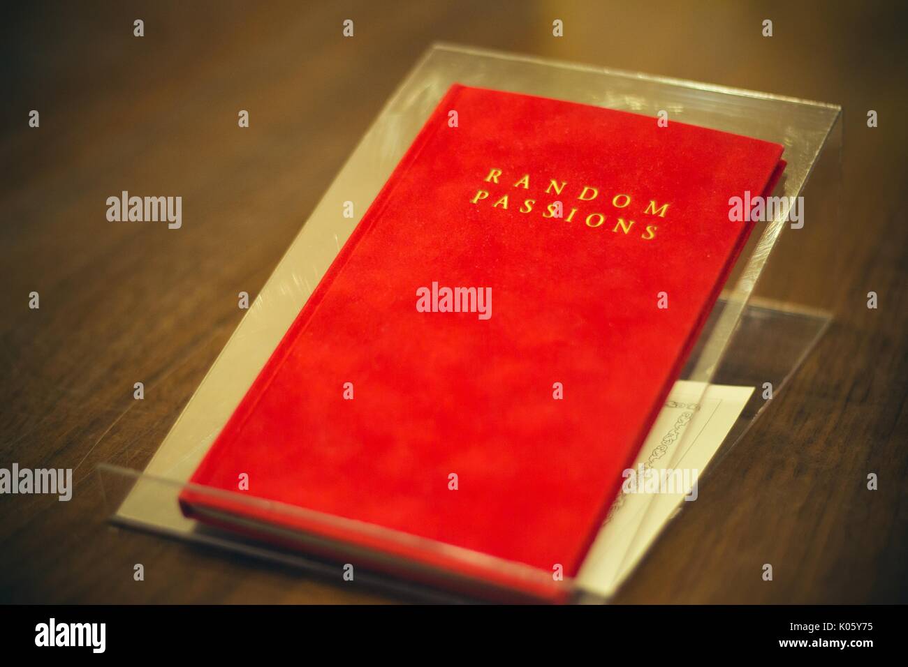 A book with a red-cover, the title 'Random Passions' written in gold, resting on a wooden table, 2016. Stock Photo