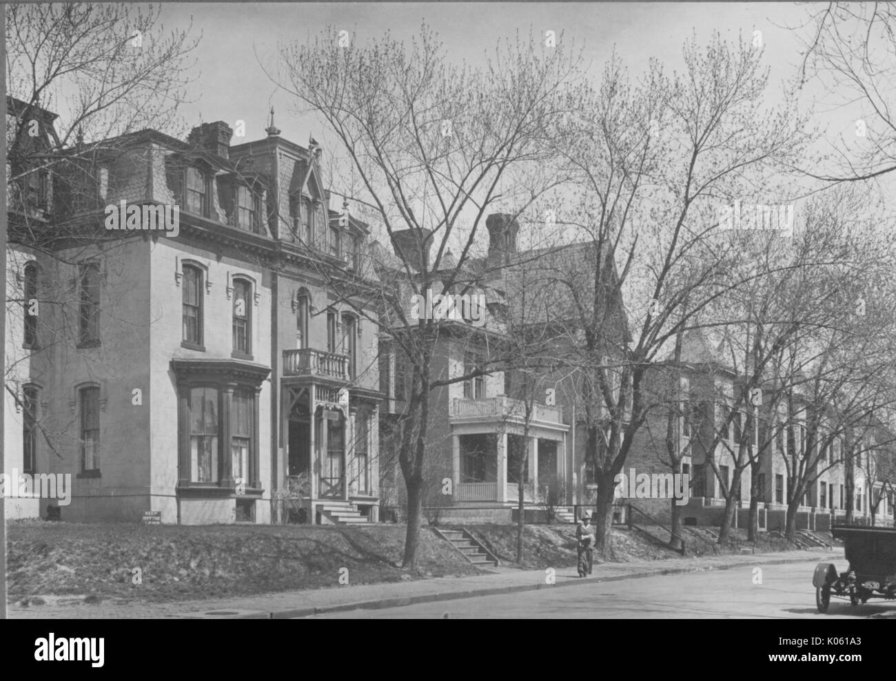 Homes parallel the street in the foreground, the homes are all at least two-story and they are very close to each other, trees lie between the street and the homes, a buggy is located in the bottom right of the photo, United States, 1950. This image is from a series documenting the construction and sale of homes in the Roland Park/Guilford neighborhood of Baltimore, a streetcar suburb and one of the first planned communities in the United States. Stock Photo