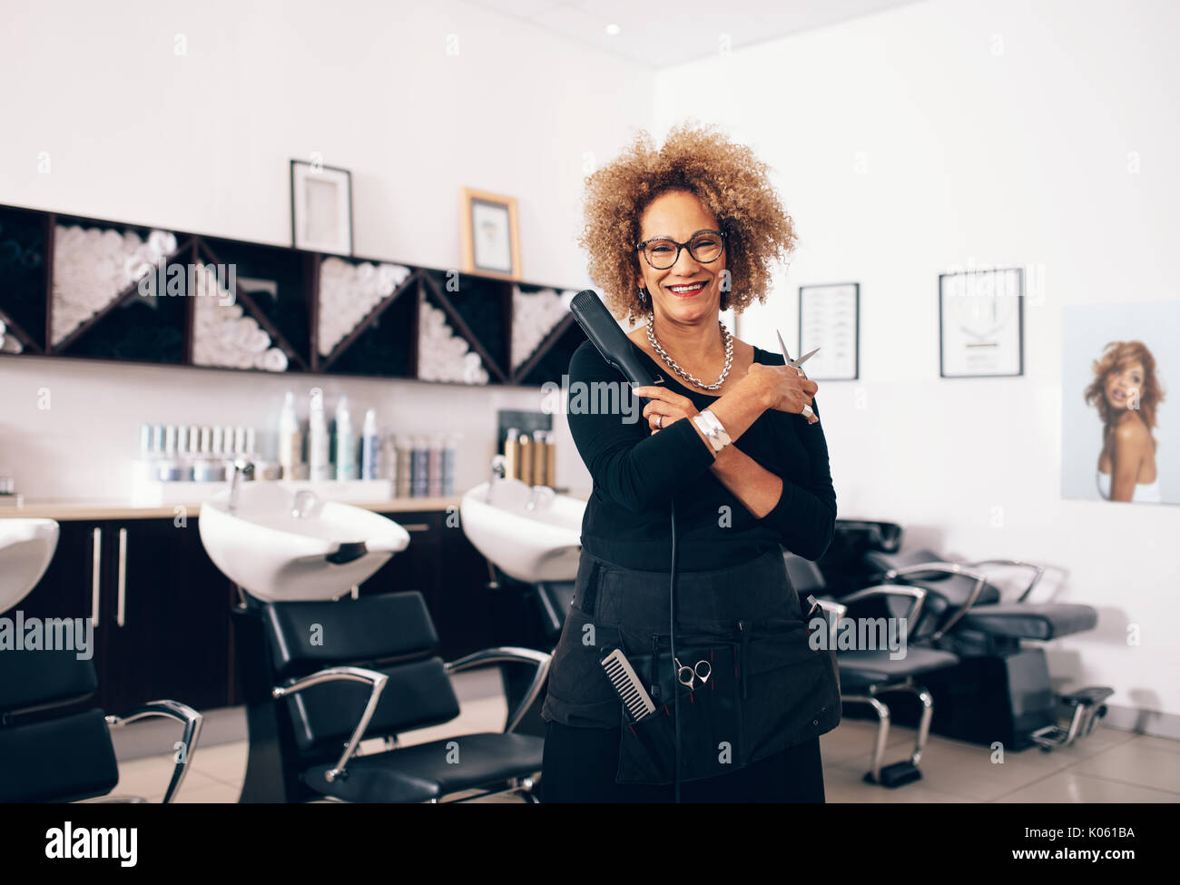 Smiling hairdresser holding a hair straightener and scissors. Well equipped  beauty salon with professional hairdresser Stock Photo - Alamy