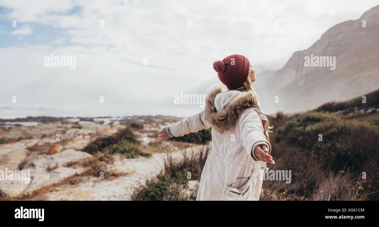 Outdoor shot of young woman on a winter day at the beach. Joyful female on a winter day with her arms outstretched along the seaside. Stock Photo