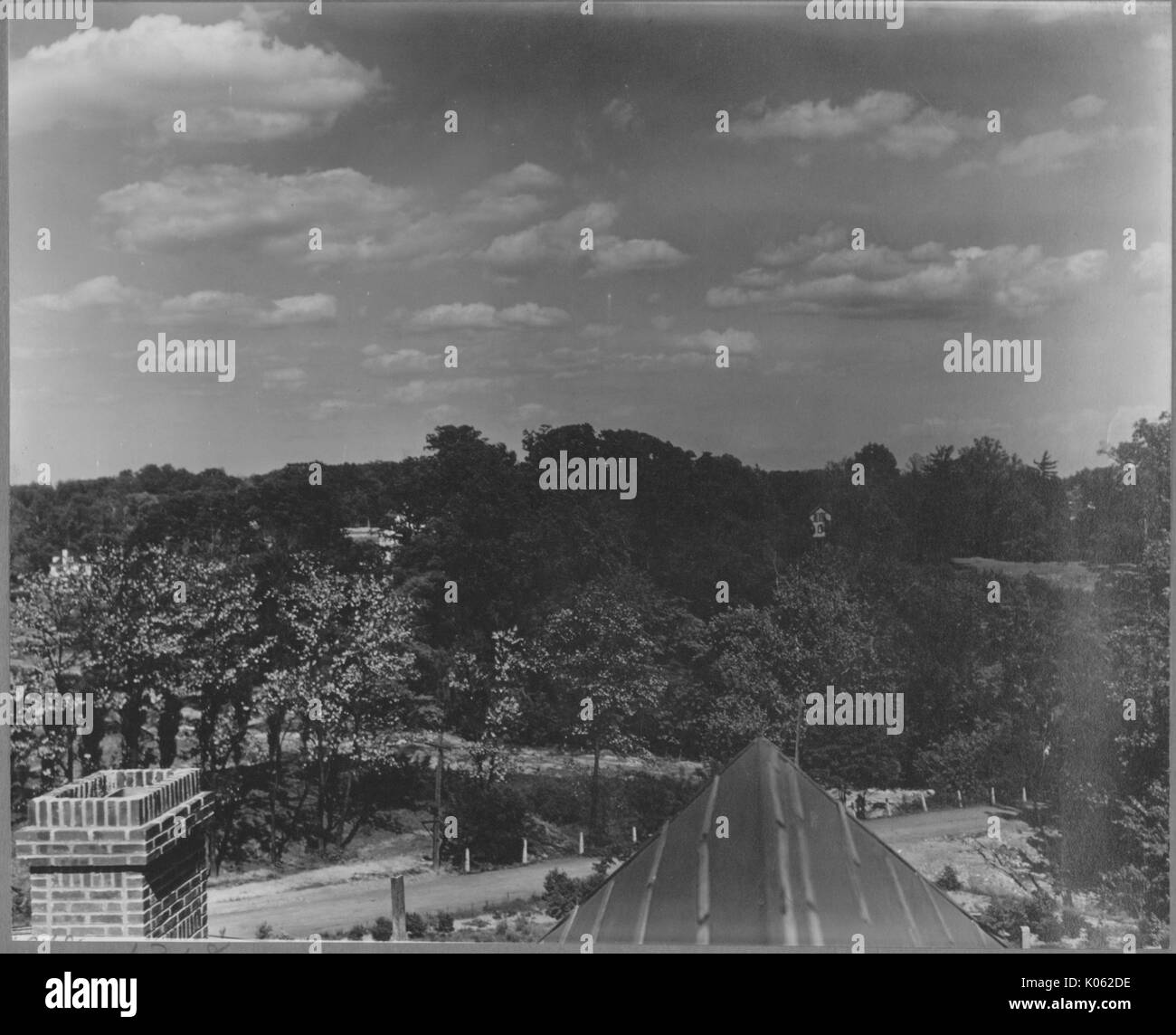 View from the roof of a house near Roland Park and Guilford, the top of a chimney and a part of the roof are in the foreground of the picture, the rest of the picture is of the street in front of the house and the trees and wilderness, the background is the sky, United States, 1910. This image is from a series documenting the construction and sale of homes in the Roland Park/Guilford neighborhood of Baltimore, a streetcar suburb and one of the first planned communities in the United States. Stock Photo