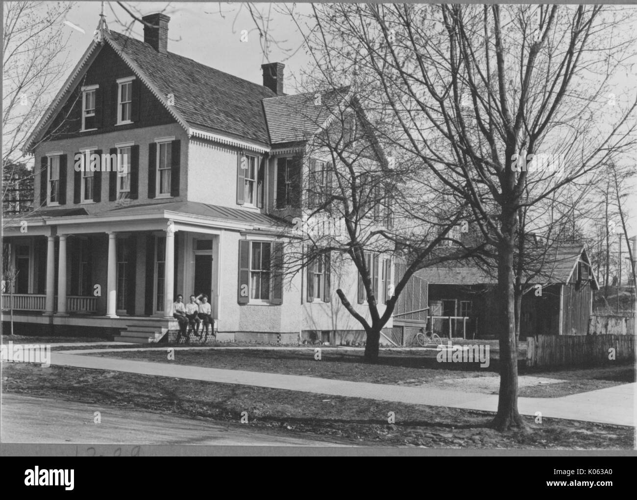 Side-angle view of a two-story single family home near Roland Park and Guilford, the house is light-colored with dark-colored window shutters, there is a porch with light-colored columns and a large wood shed in the backyard, United States, 1910. This image is from a series documenting the construction and sale of homes in the Roland Park/Guilford neighborhood of Baltimore, a streetcar suburb and one of the first planned communities in the United States. Stock Photo