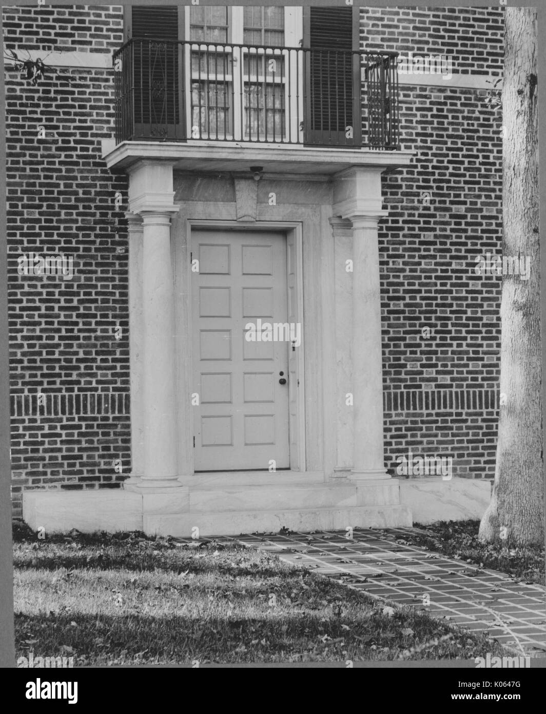 Light-colored front door with a window with shutters above it near Roland Park and Guilford, the building is brick, there are two light-colored columns to the sides of the front door and a pathway leading to it, United States, 1910. This image is from a series documenting the construction and sale of homes in the Roland Park/Guilford neighborhood of Baltimore, a streetcar suburb and one of the first planned communities in the United States. Stock Photo