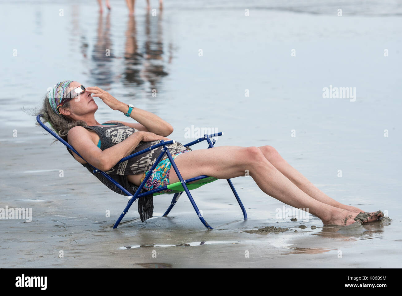 Charleston, Isle of Palms, USA. 21st Aug, 2017. A woman relaxes in a beach chair as she view the total solar eclipse over the beach outside Charleston August 21, 2017 in Isle of Palms, South Carolina. The solar eclipse after sweeping across the nation crosses the Charleston area before heading over the Atlantic Ocean. Credit: Planetpix/Alamy Live News Stock Photo