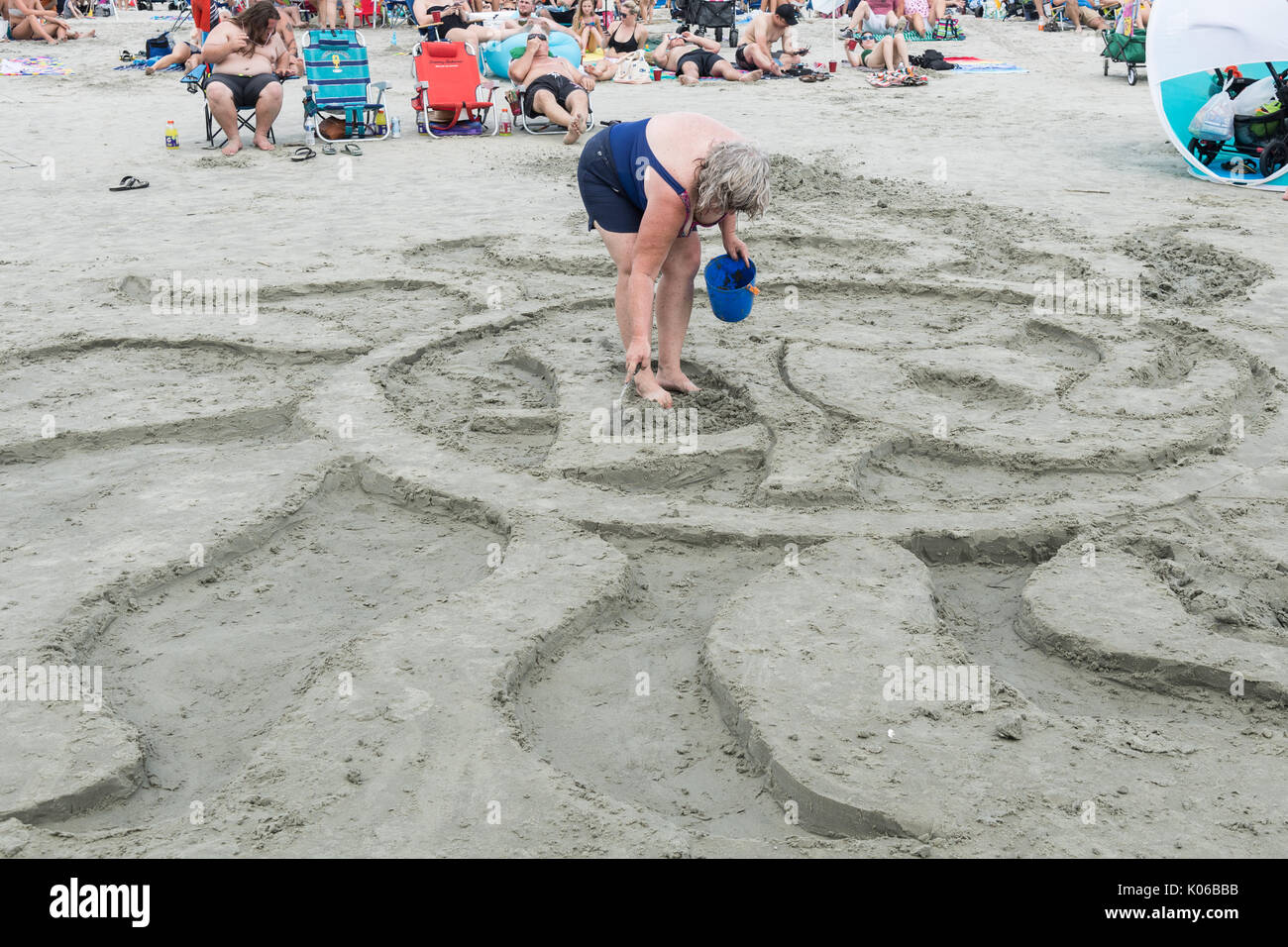 Charleston, Isle of Palms, USA. 21st Aug, 2017. A woman finishes a design in the sand to celebrate the total solar eclipse as thousands gather on the beach outside Charleston August 21, 2017 in Isle of Palms, South Carolina. The solar eclipse after sweeping across the nation crosses the Charleston area before heading over the Atlantic Ocean. Credit: Planetpix/Alamy Live News Stock Photo