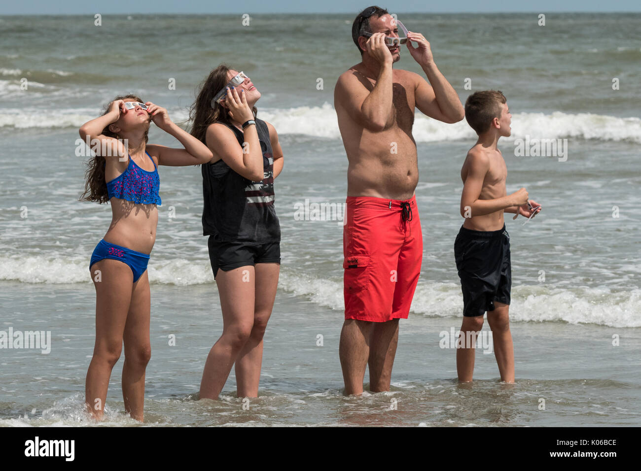 Charleston, Isle of Palms, USA. 21st Aug, 2017. A family stands in the water as they view the total solar eclipse as it passes over the beach outside Charleston August 21, 2017 in Isle of Palms, South Carolina. The solar eclipse after sweeping across the nation crosses the Charleston area before heading over the Atlantic Ocean. Credit: Planetpix/Alamy Live News Stock Photo