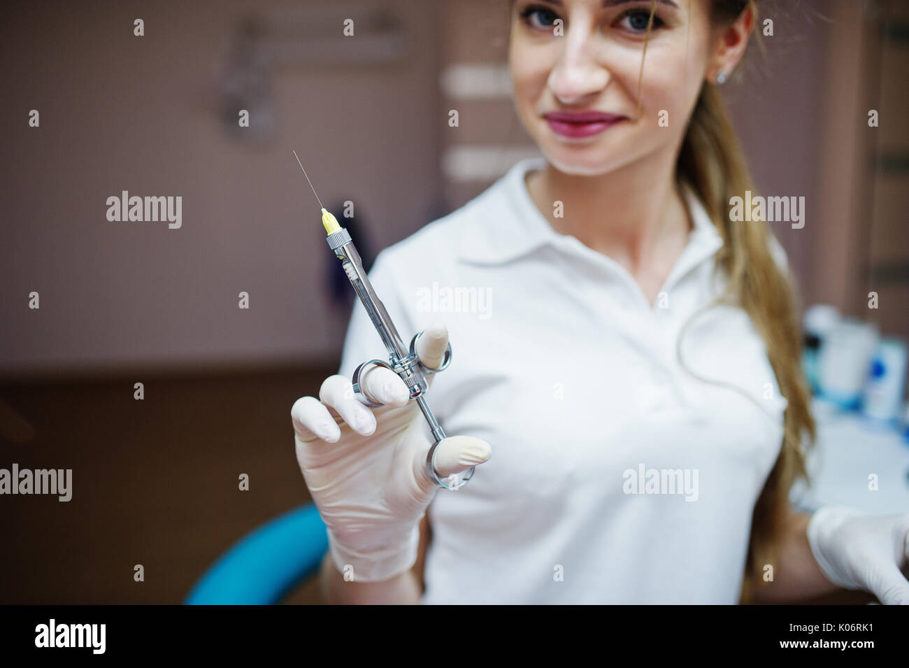 Portrait of a female dentist in white coat posing with syringe filled