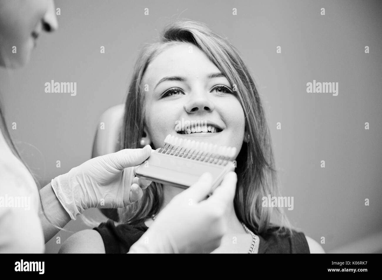 Talented female dentist figuring out what is the matching teeth color for her patient. Black and white photo. Stock Photo