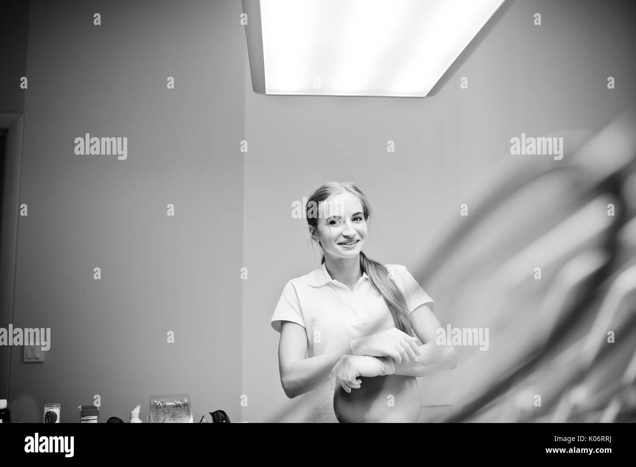 Good-looking female dentist posing in white coat in a modern well-equipped cabinet. Black and white photo. Stock Photo