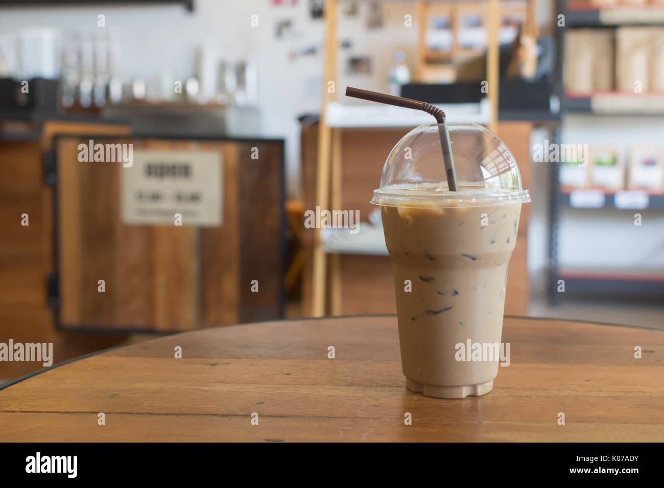 iced latte with straw in plastic cup on wood table in coffee shop