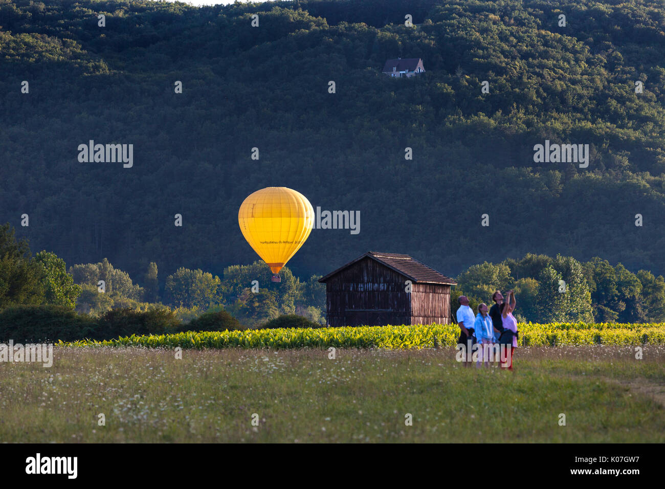 A Hot Air Balloon Illuminated by the Setting Sun with a Group of People Looking Skywards, Dordogne, France, Europe. Stock Photo