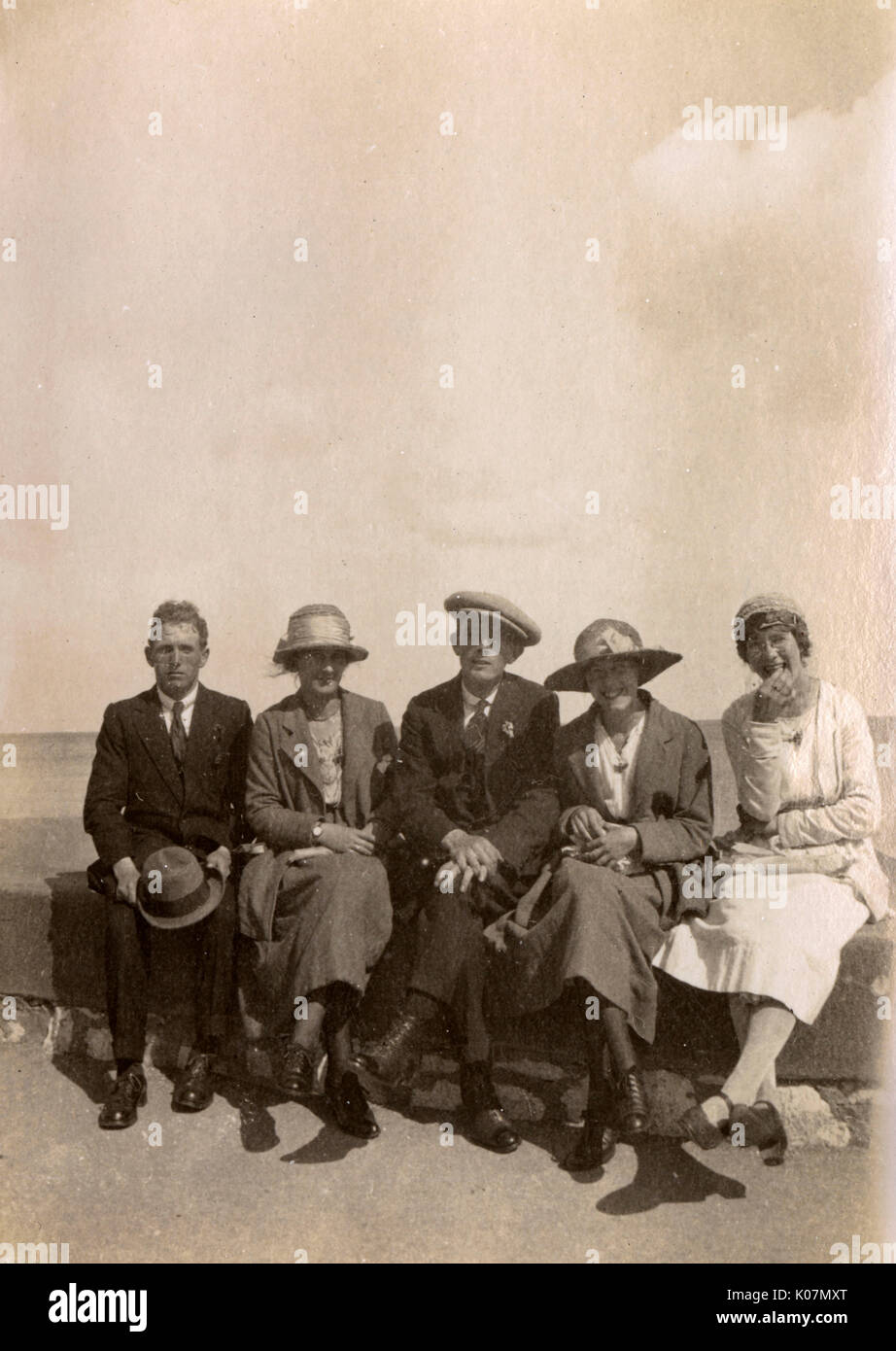 Five people sitting on a wall at the seaside Stock Photo