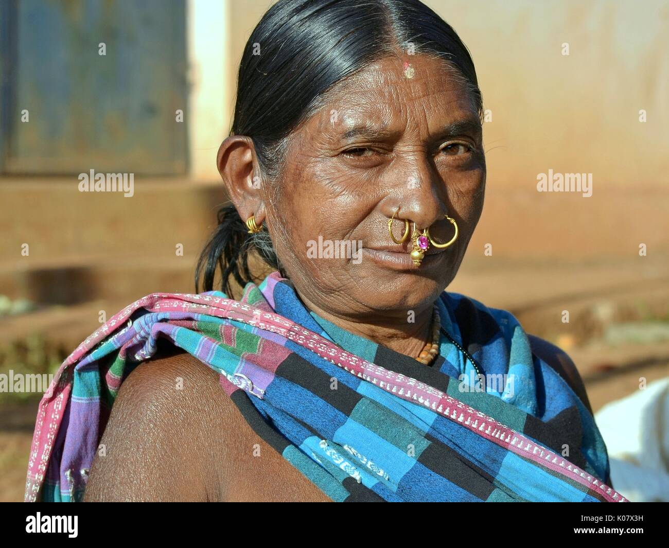 Elderly Indian Adivasi woman with two golden nose rings, precious gold-and-gemstone nose jewellery and tribal earrings poses for the camera. Stock Photo