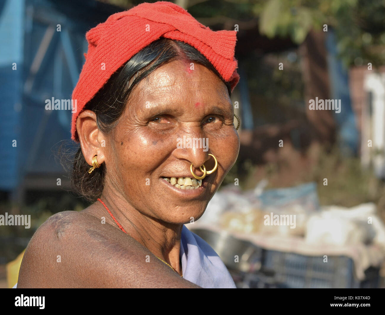Elderly Indian Adivasi woman with two golden nose rings and distinctive tribal earrings smiles for the camera. Stock Photo