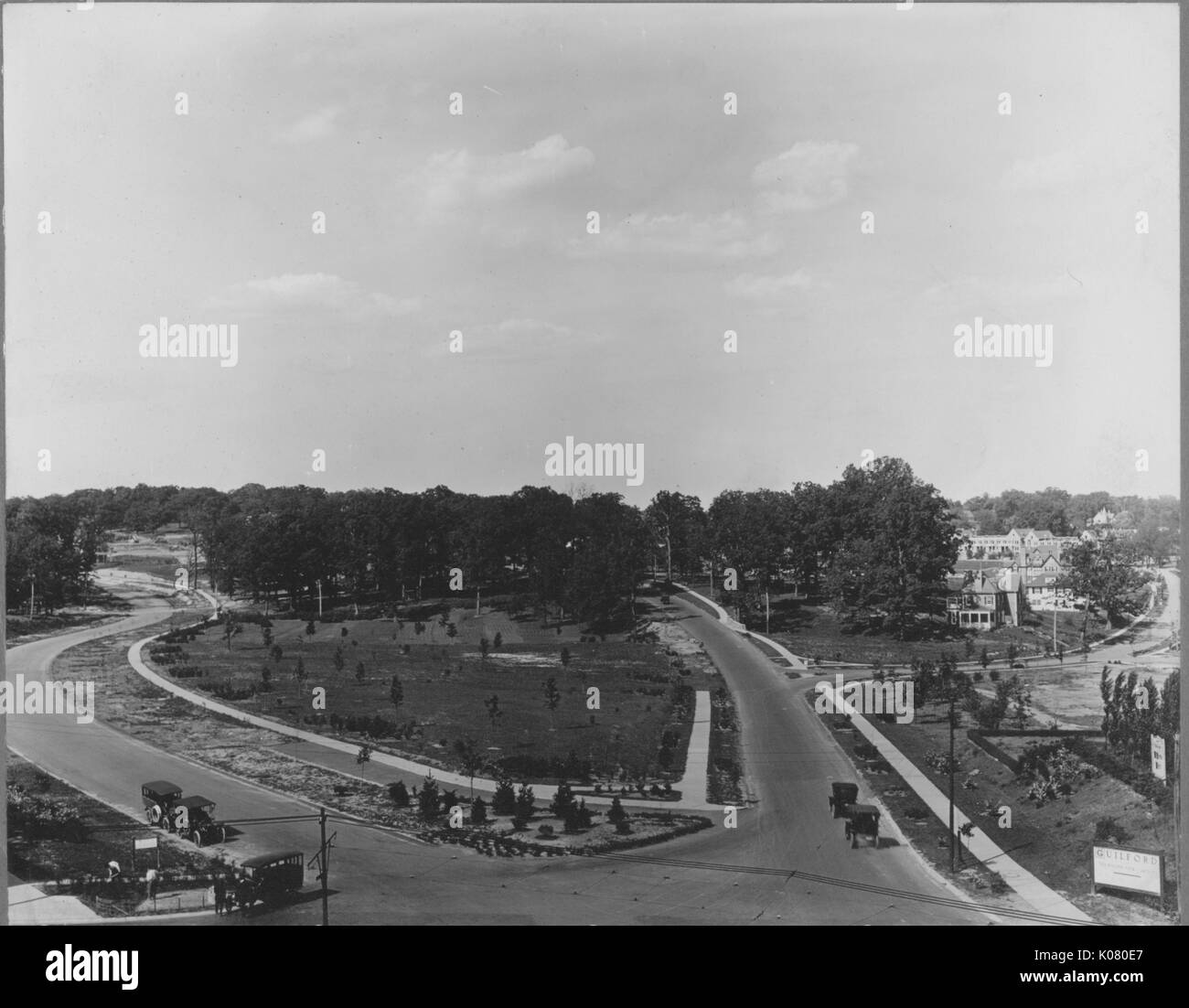 Aerial shot of two streets with sidewalks intersecting, with some cars depicted, trees in the background, Roland Park/Guilford, United States, 1910. This image is from a series documenting the construction and sale of homes in the Roland Park/Guilford neighborhood of Baltimore, a streetcar suburb and one of the first planned communities in the United States. Stock Photo