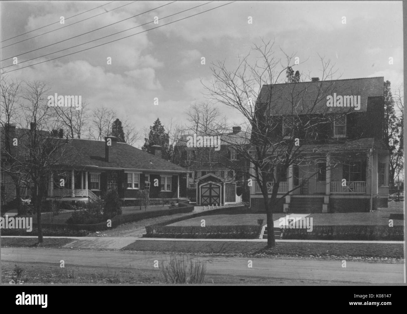 Front view of several single-family homes near Roland Park and Guilford, the homes are all dark-colored, two of them are two story and one is one story, United States, 1910. This image is from a series documenting the construction and sale of homes in the Roland Park/Guilford neighborhood of Baltimore, a streetcar suburb and one of the first planned communities in the United States. Stock Photo