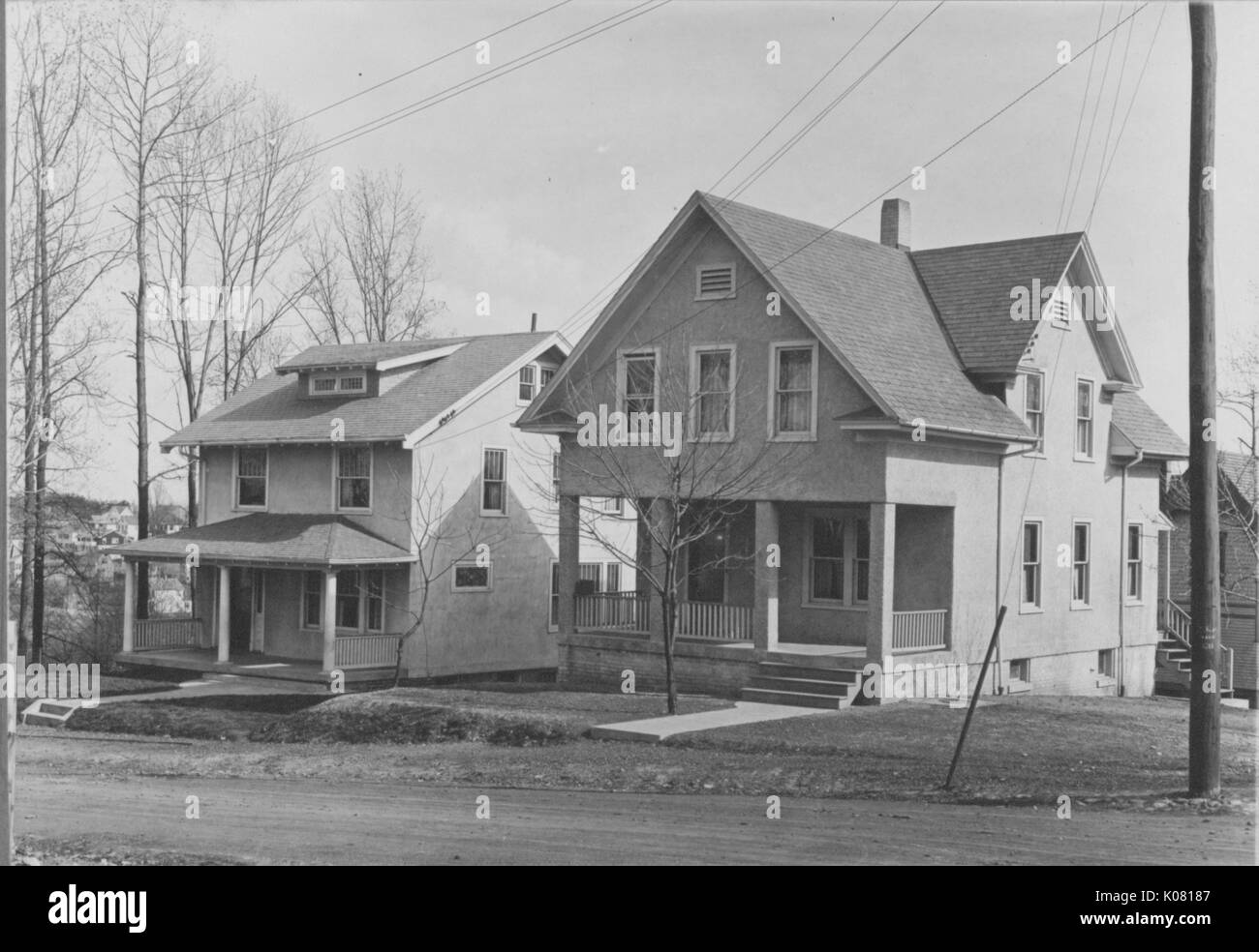 Photograph of two Roland Park homes in Baltimore, both two-story homes with spacious porches, located on a hill, neither made of brick, but with large Baltimore-styled windows, besides trees with no leaves, United States, 1920. This image is from a series documenting the construction and sale of homes in the Roland Park/Guilford neighborhood of Baltimore, a streetcar suburb and one of the first planned communities in the United States. Stock Photo