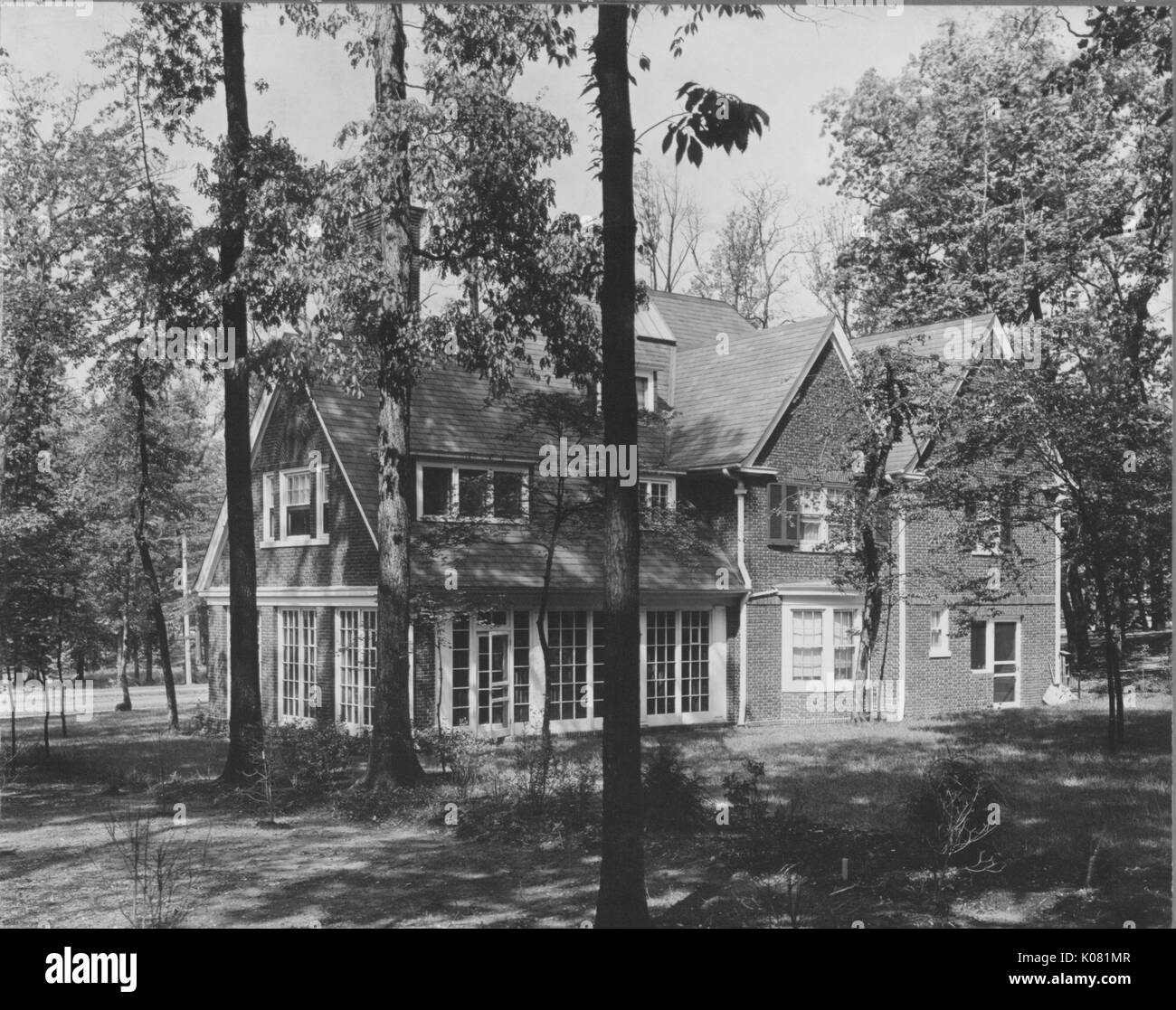 Exterior of a large brick home, featuring many large windows, situated among many trees on a quiet road in Baltimore, Maryland, 1910. This image is from a series documenting the construction and sale of homes in the Roland Park/Guilford neighborhood of Baltimore, a streetcar suburb and one of the first planned communities in the United States. Stock Photo