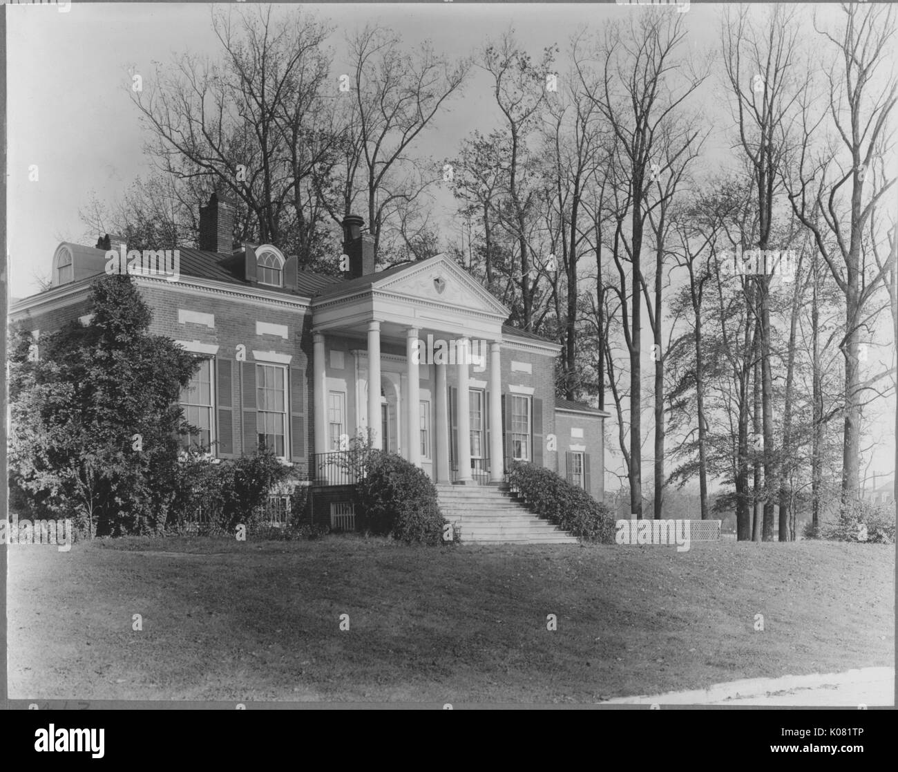 Photograph of Homewood Museum located on the Johns Hopkins campus, a small one-story brick building with four Doric columns in front, large windows, located on a grassy quad, besides some large trees that have lost their leaves, United States, 1950. This image is from a series documenting the construction and sale of homes in the Roland Park/Guilford neighborhood of Baltimore, a streetcar suburb and one of the first planned communities in the United States. Stock Photo