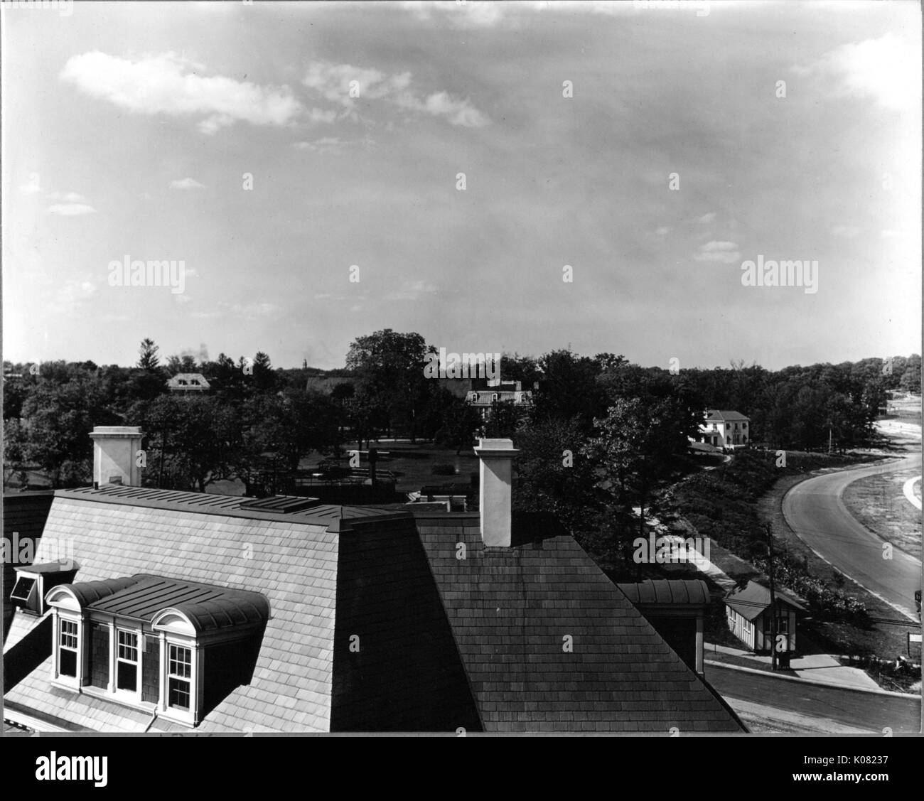 Aerial shot of a neighborhood in Baltimore, Maryland, showing the roof of a house with dormer windows and two chimneys, a road, many trees, and partially-obscured homes in the background, 1910. Stock Photo
