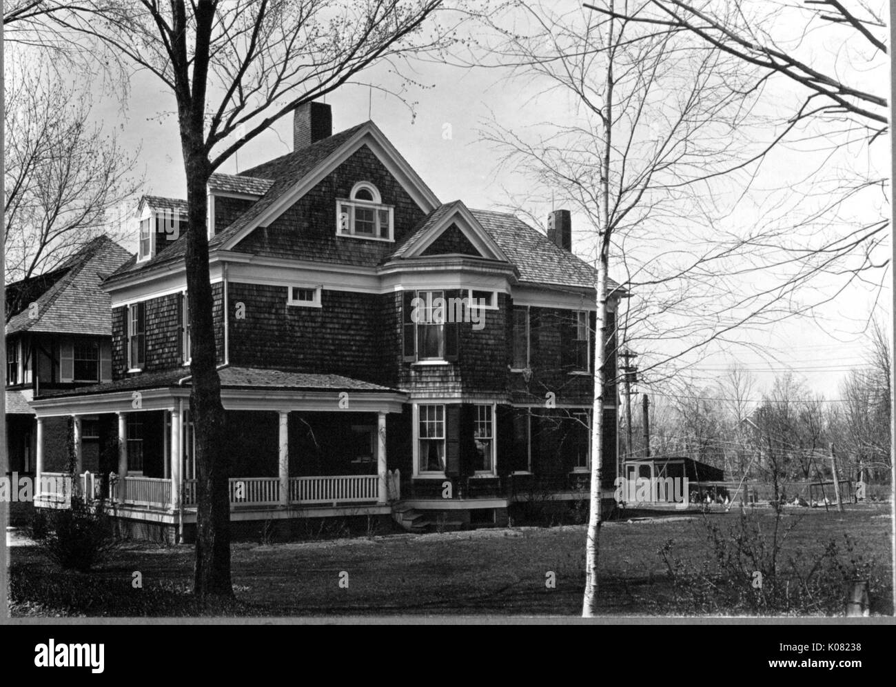 A large single-family home with a large front porch, dormer windows, cedar shingles, chimneys, and and large yard with shrubbery in trees in Baltimore, Maryland, 1910. Stock Photo