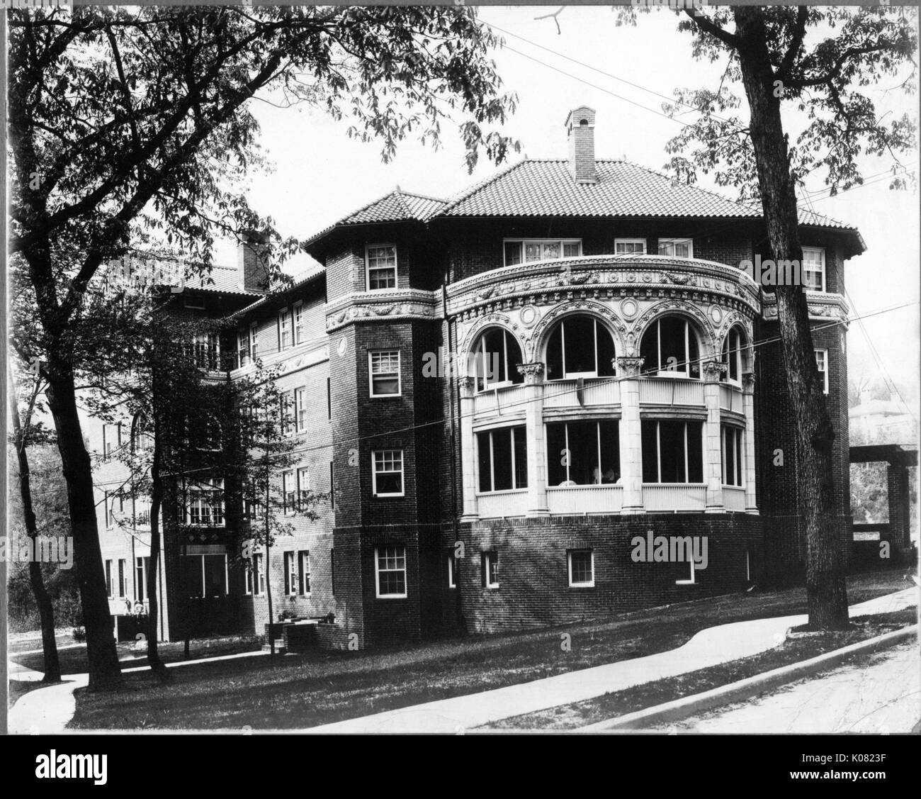 A large, four-story brick building with ornate stone accents, possibly a home, situated among trees on a street with a sidewalk in Baltimore, Maryland, 1910. Stock Photo