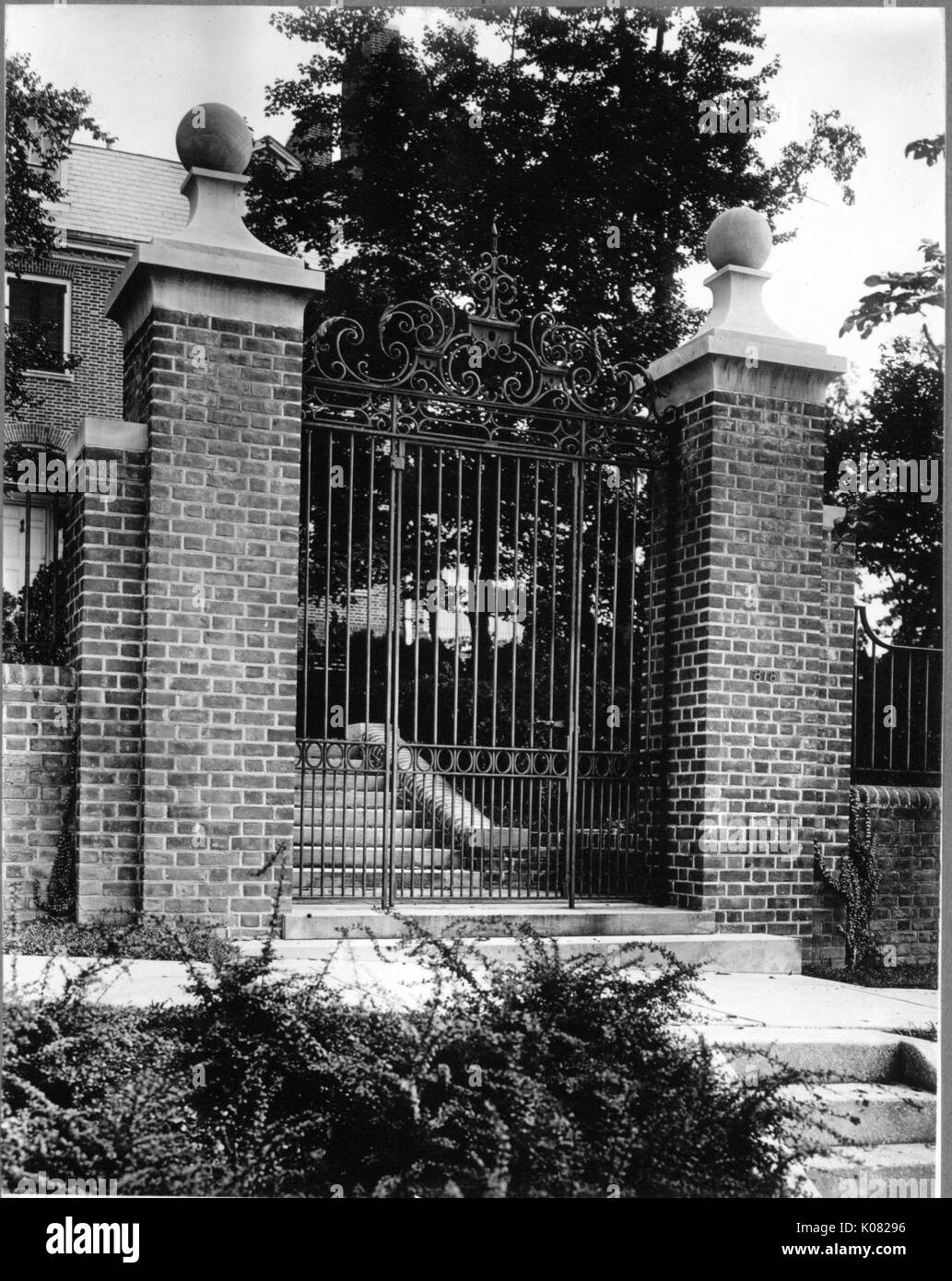 An ornate gate with brick pillars sits between two sets of steps, which lead to a brick home in Baltimore, Maryland, 1910. This image is from a series documenting the construction and sale of homes in the Roland Park/Guilford neighborhood of Baltimore, a streetcar suburb and one of the first planned communities in the United States. Stock Photo