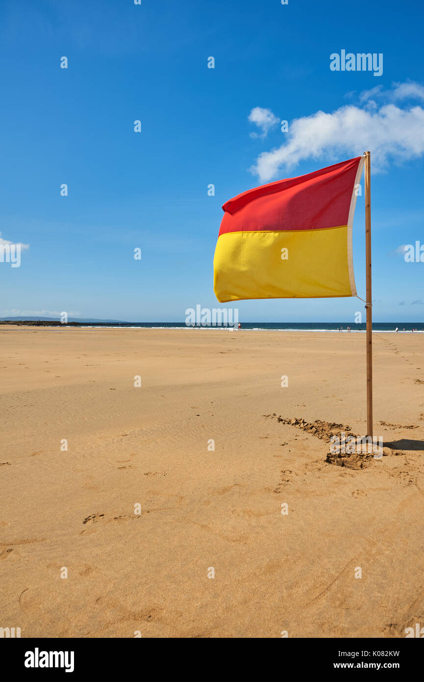 Red and yellow warning flag against a blue sky advising swimmers on the beach at Ballybunion, County Kerry Ireland Stock Photo