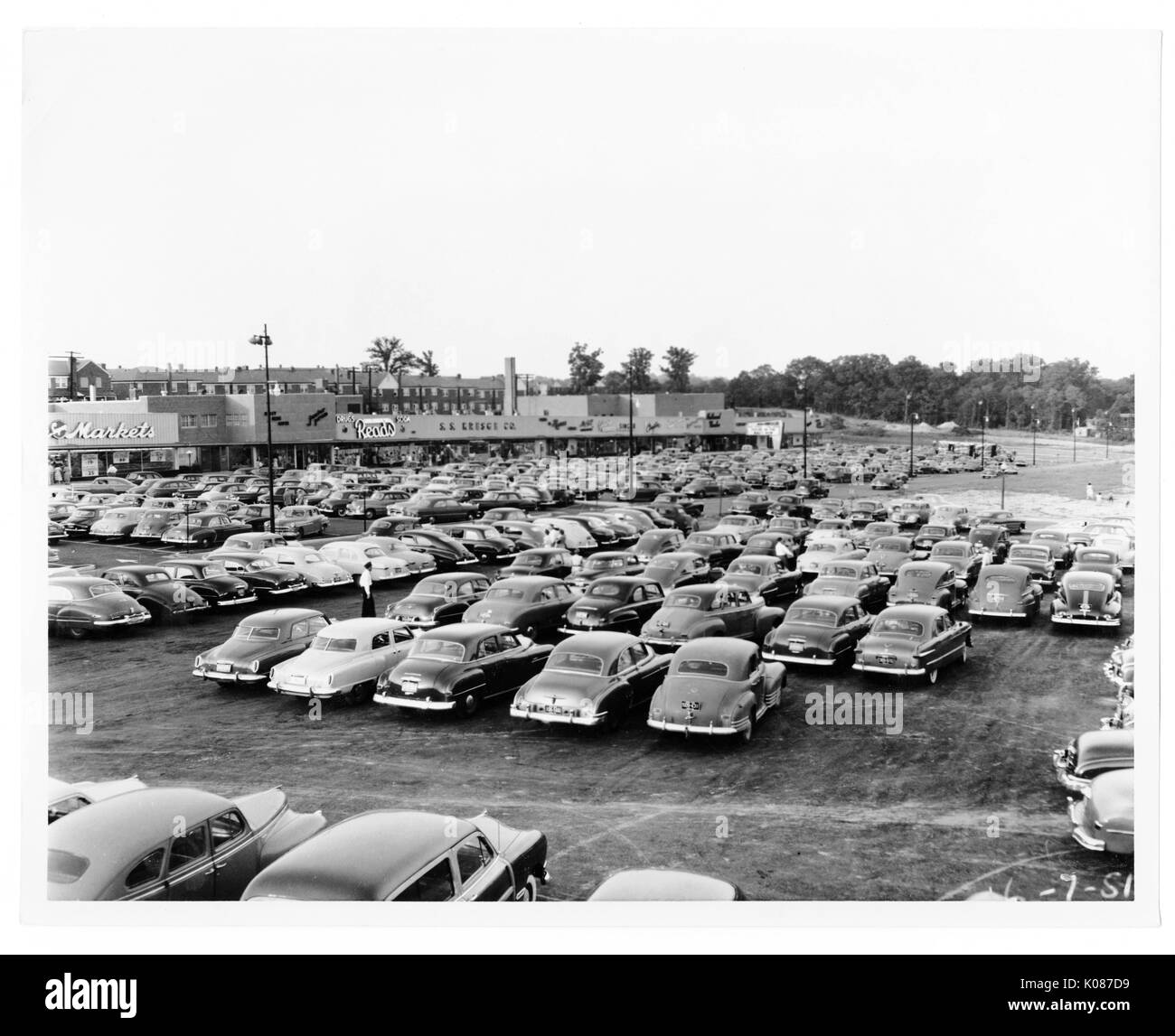 Parking lot of Northwood Shopping Center with hundreds of cars, stores in background including Acme Markets and Reads, trees and homes in background, parking lot has many city lights, Baltimore, Maryland, 1930. Stock Photo