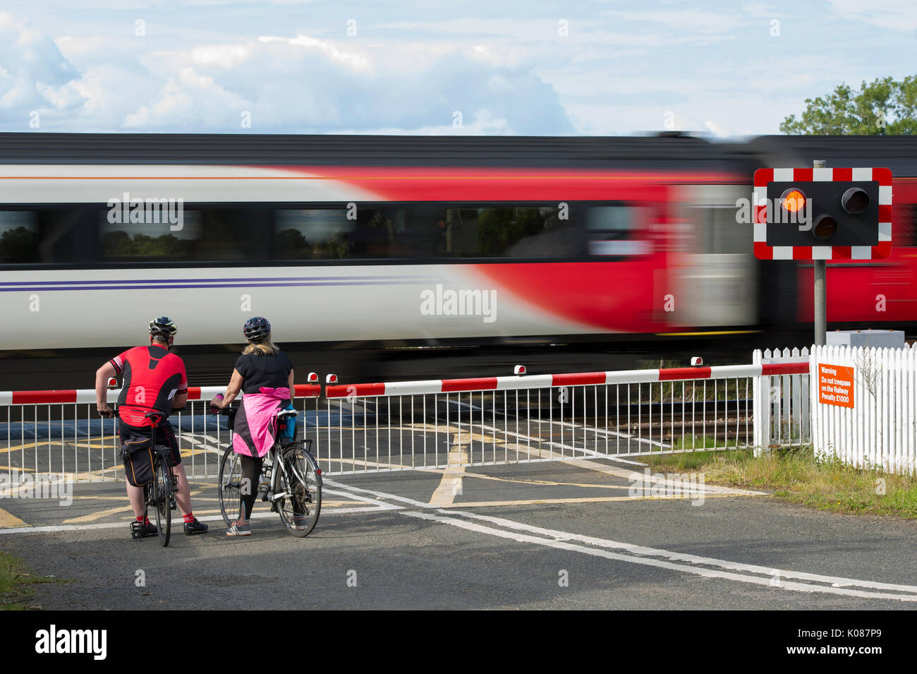 Two cyclists wait for a Virgin train to pass at a level crossing on the East Coast main line near Aberlady, East Lothian Stock Photo