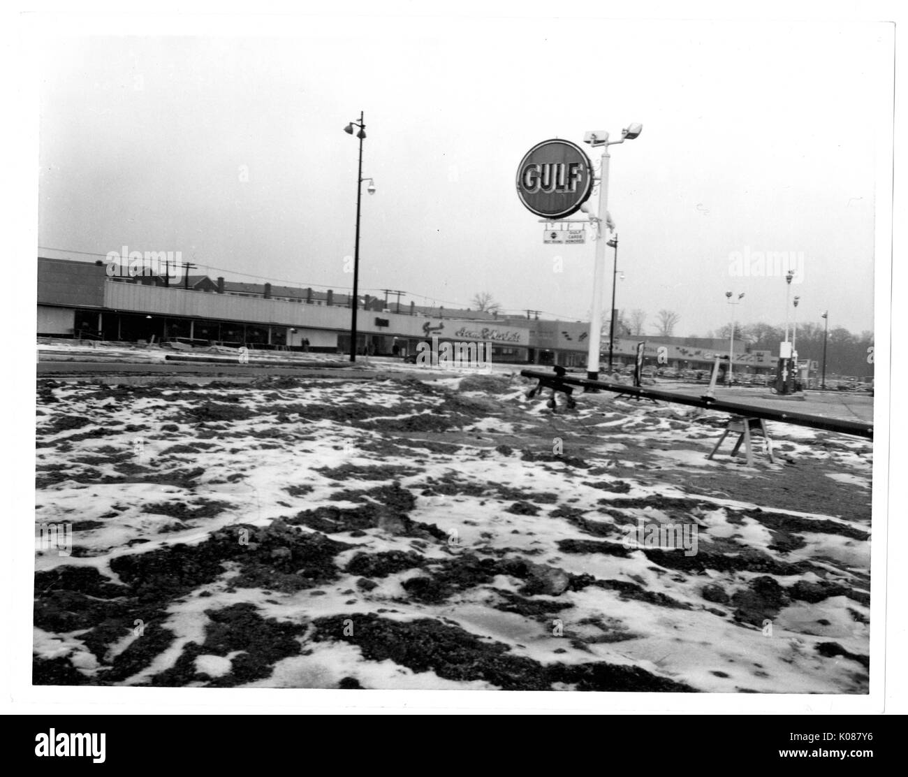 View of snow on top of dirt at a construction zone, there is a large GULF gas station sign by the construction zone and there is a shopping center in the background, across the street, Baltimore, Maryland, 1951. Stock Photo
