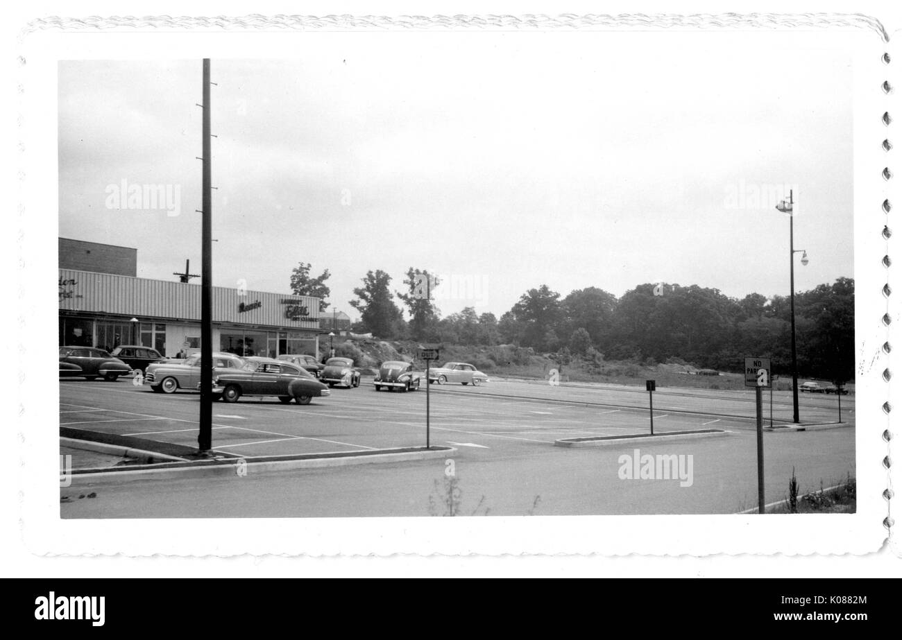 Across the street is a shopping center with several stores, the parking lot is not very full, trees line the perimeter of the parking lot on one side, Baltimore, Maryland, 1951. Stock Photo