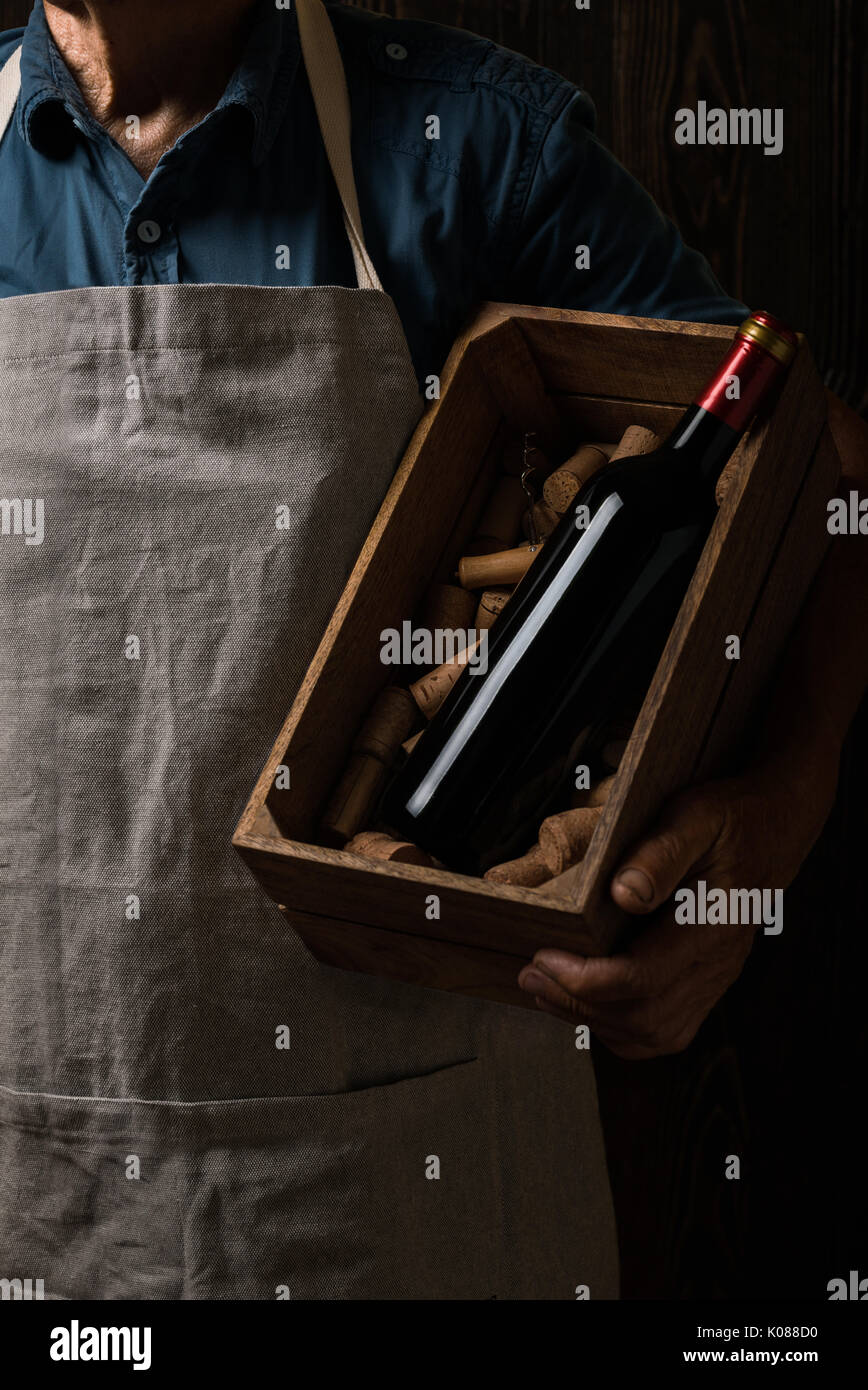 Old winemaker holding a wooden box with bottle of red wine Stock Photo