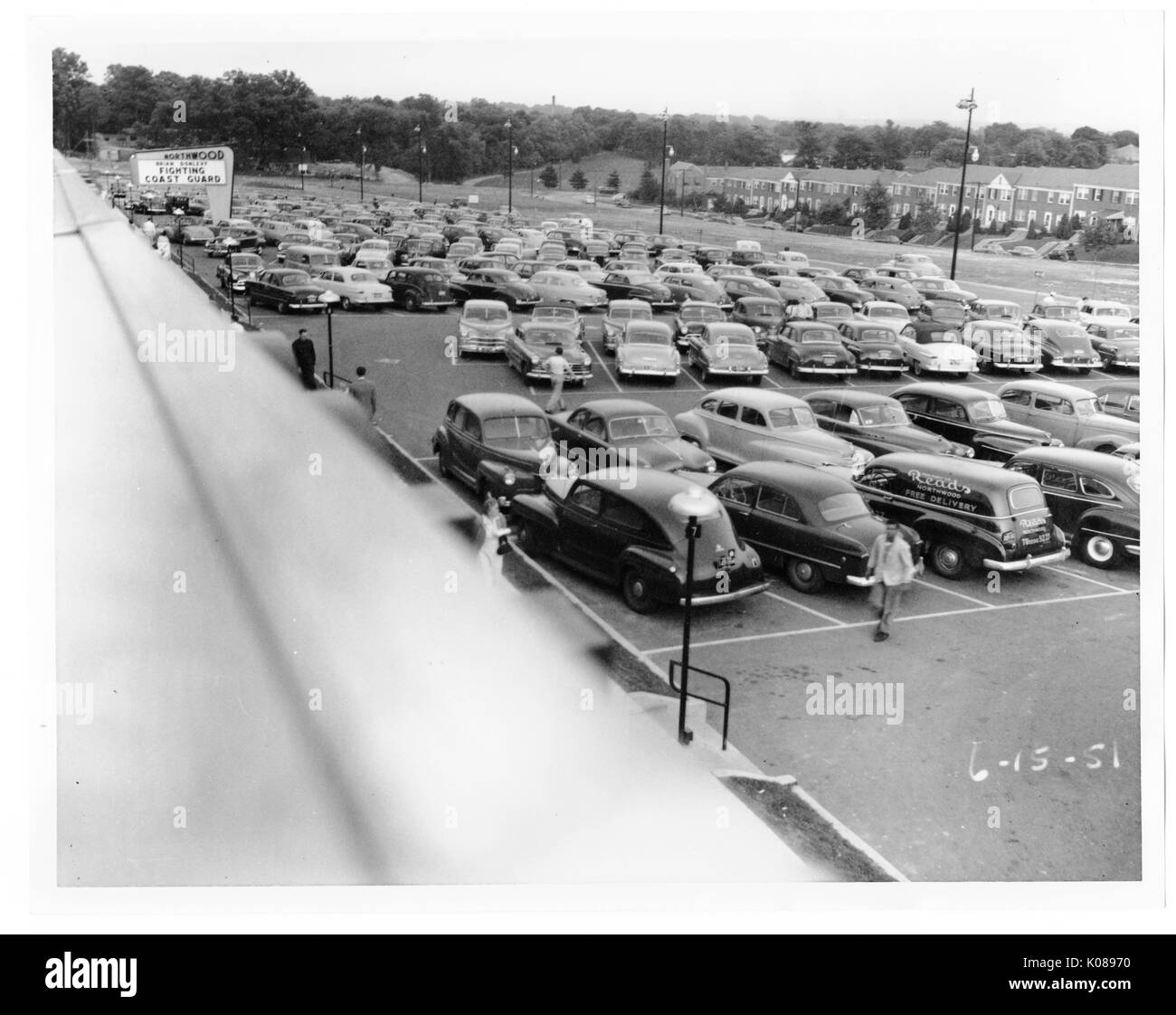 View of a packed parking lot from the roof of the Northwood Shopping Center, across the street from the center and parking lot are brick row homes, people are walking to and from their cars, the center's sign is advertising 'FIGHTING COAST GUARD', Baltimore, Maryland, 1951. Stock Photo