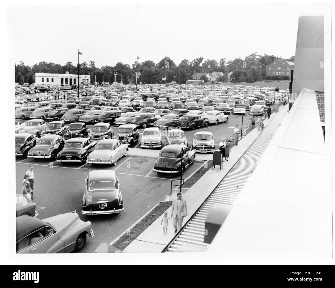 Photograph of parking lot for the Northwood Shopping Center in Baltimore, Maryland, full of cars, with patrons walking on the sidewalks, residential and commercial buildings and trees in the background, Baltimore, Maryland, 1951. Stock Photo