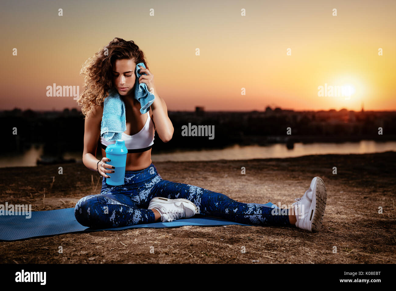Young fitness woman resting afther hard training on the city rooftop at sunset. Stock Photo