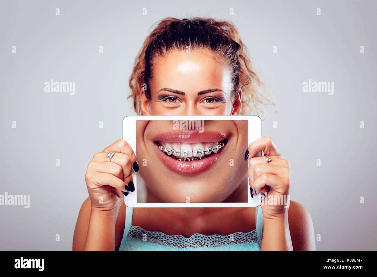 Smiling girl with braces on teeth behind digital tablet. Looking at camera. Stock Photo