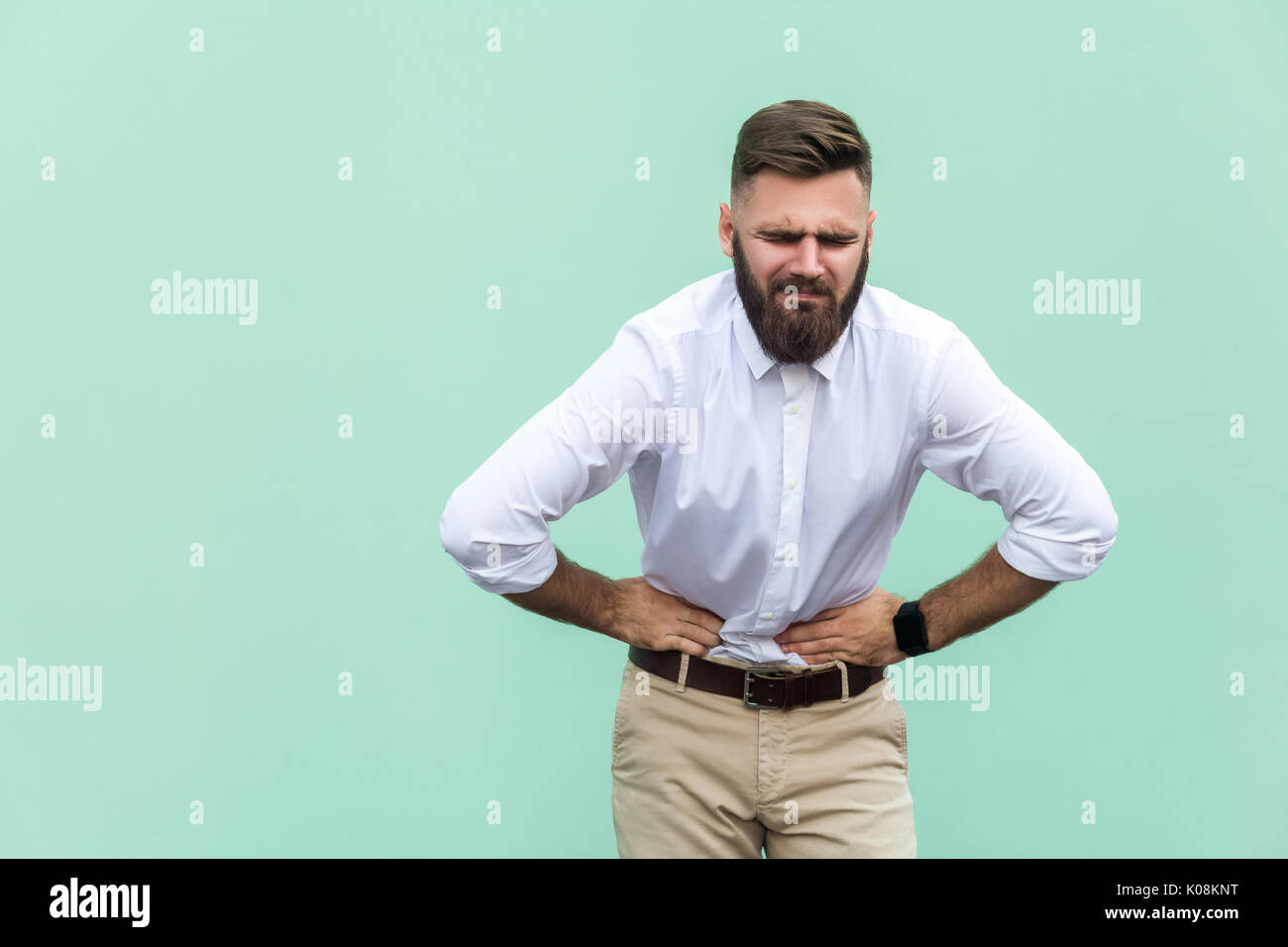 Bad  emotions and feelings, pain. Young man, experiencing stomach pain, isolated on light green background. Indoor, studio shot Stock Photo