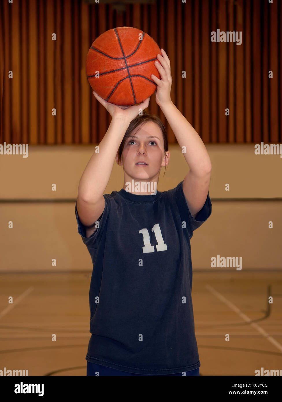 A young woman shoots a basketball in a gym. Stock Photo