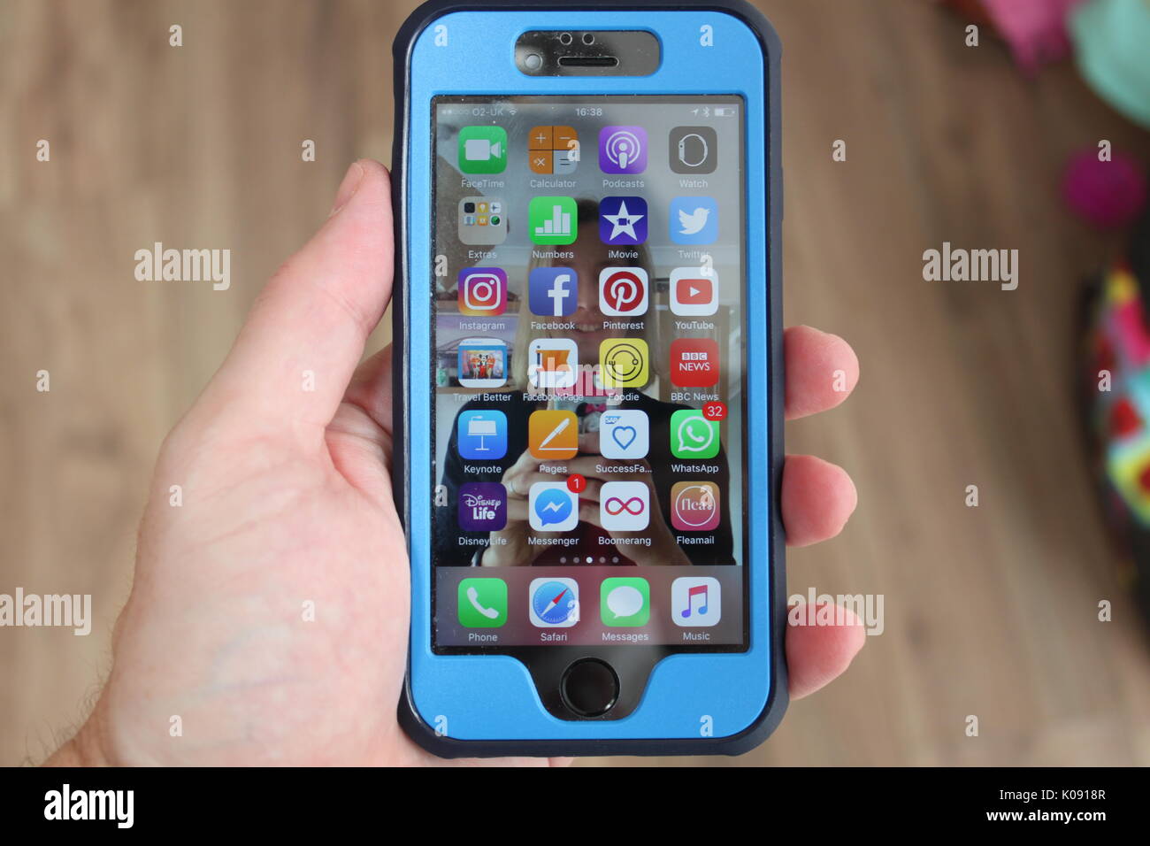 iPhone with a protective blue cover from Anker held in a mans hand showing apps and notifications on the screen Stock Photo