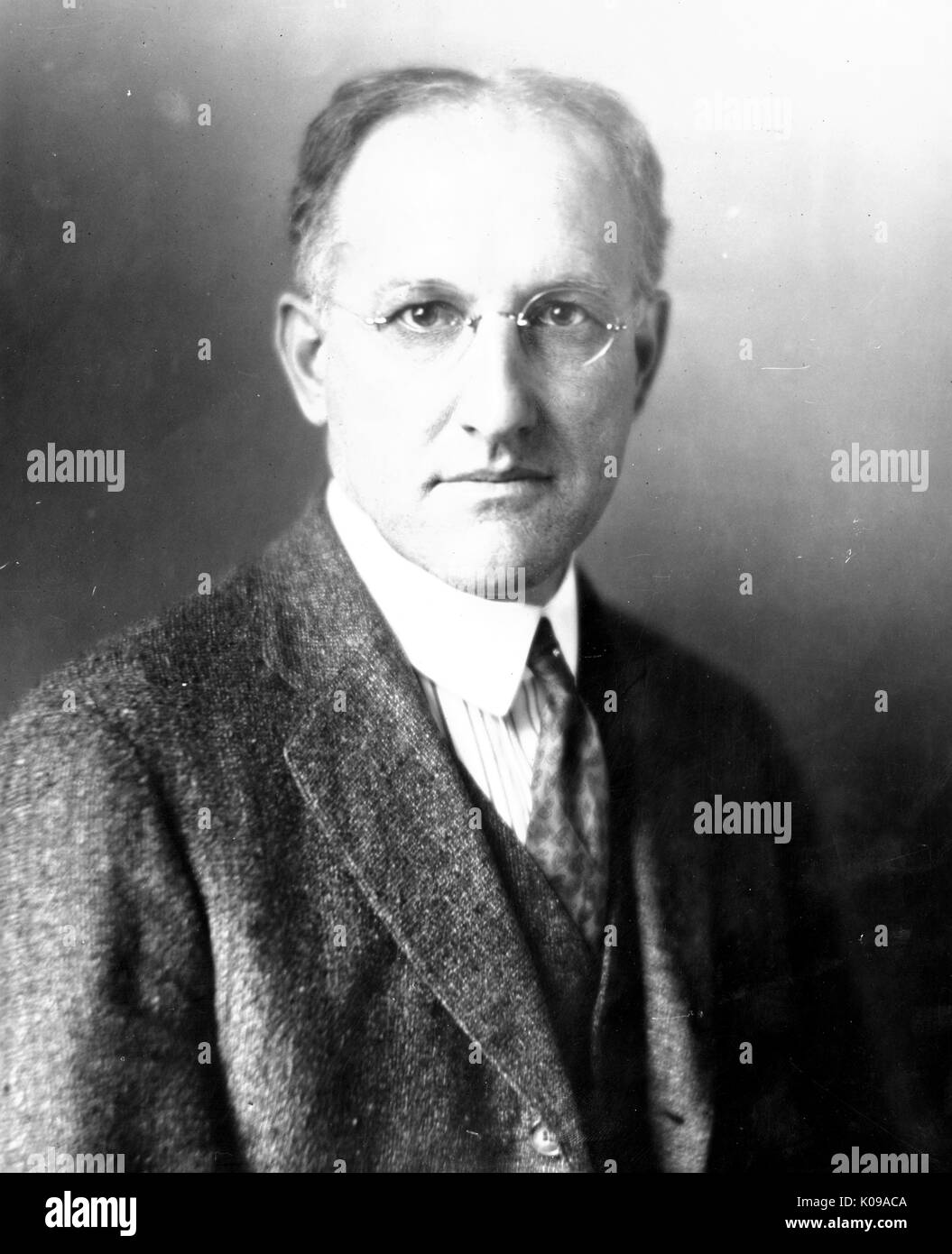 Half-length of Dr. Samuel Mast, biology faculty member at the Johns Hopkins University, wearing a dark three piece suit and a dark tie with a striped shirt and circular glasses with no rim, in front of a backdrop, with a serious facial expression. 1935. Stock Photo