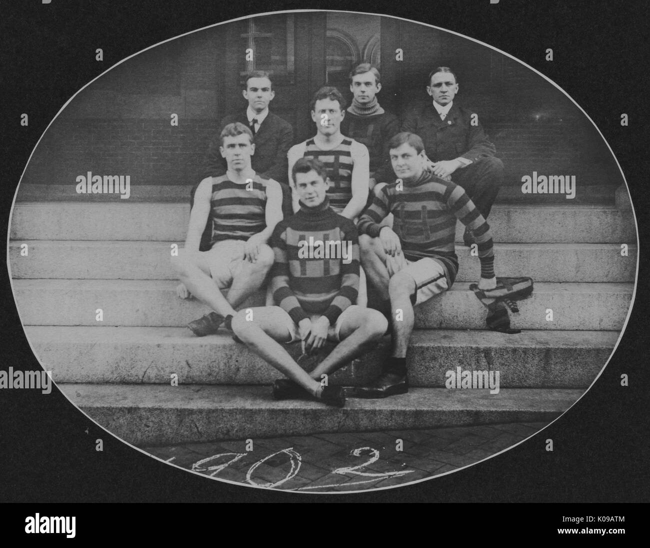 Group photograph, members of the track team are seated in uniform in a formal portrait on the steps, 1902. Stock Photo