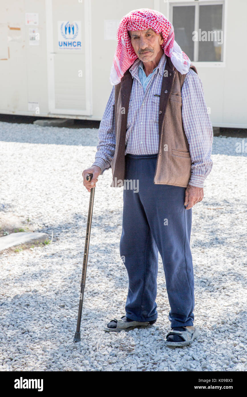 An older Syrian man supported by a walking stick stands in front of a prefabricated office building with a UNHCR sign. UN High Commission for Refugees Stock Photo