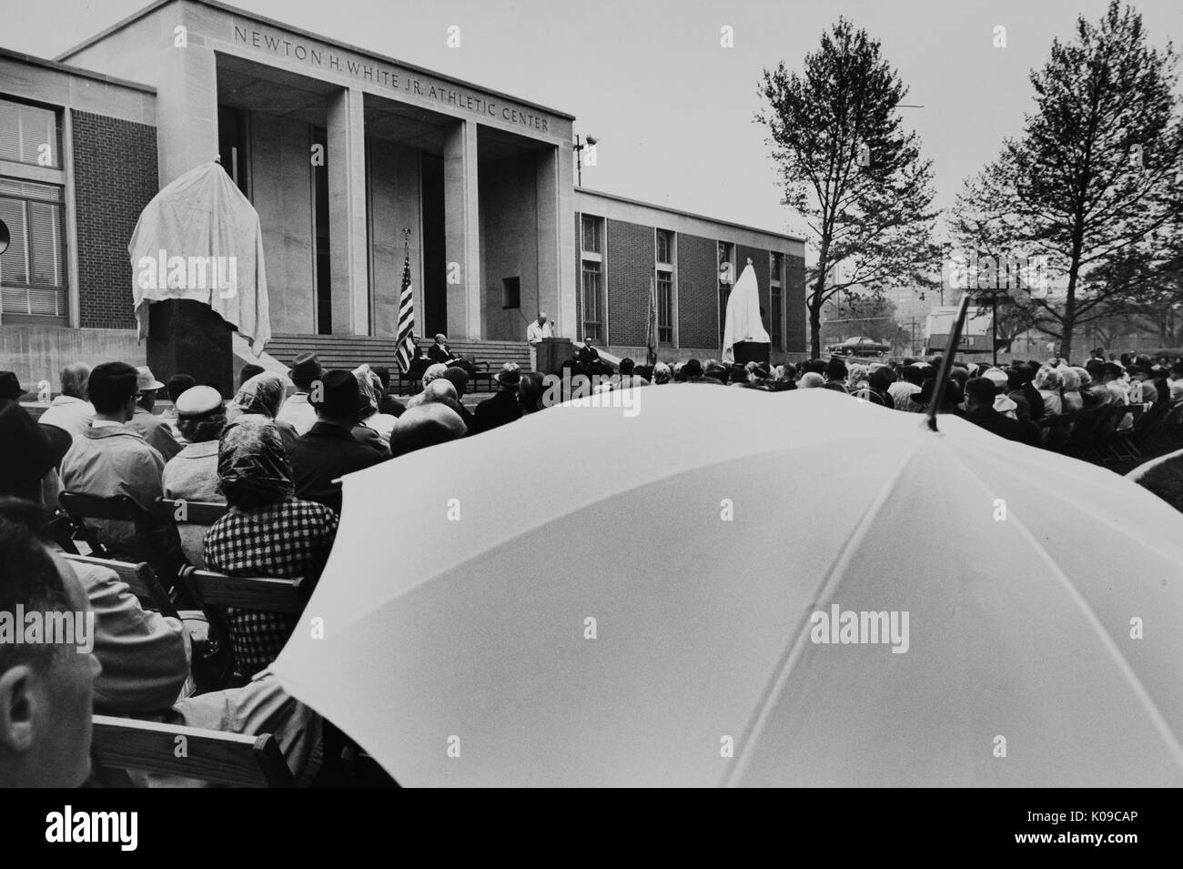 A speech is being given in front of the Newton H White, Jr, Athletic Center  at The Johns Hopkins University, the athletic center was expanded and  renamed Newton H White, Jr, Athletic