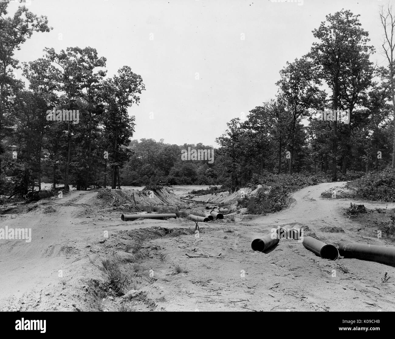 Northwood neighborhood land under construction, there are large pipes scattered on the uneven dirt, there are trees and bushes in the background that are bordering the land, United States, 1950. Stock Photo
